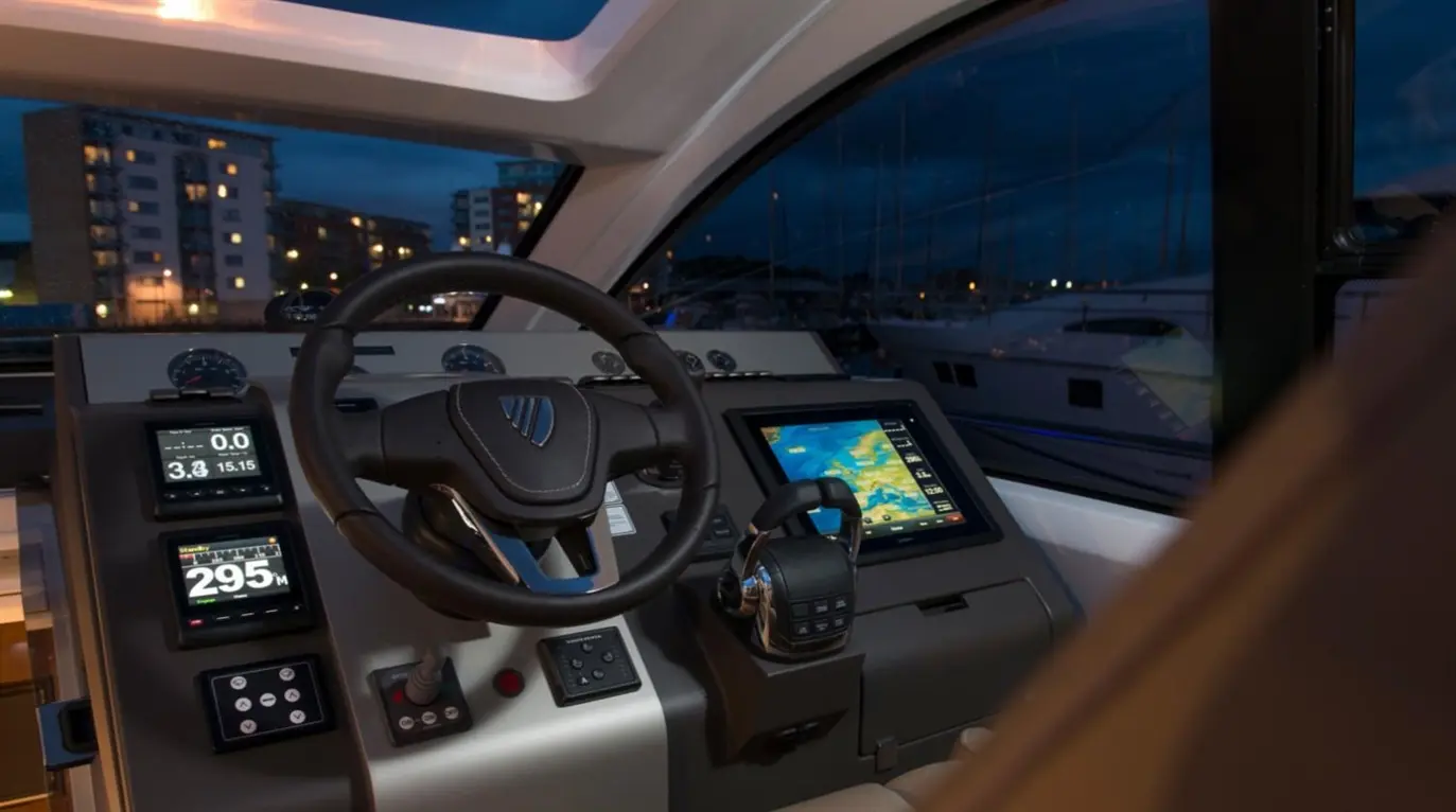 Cockpit of a luxury boat at night, featuring navigation screens displaying map and stats, with steering wheel and controls visible.